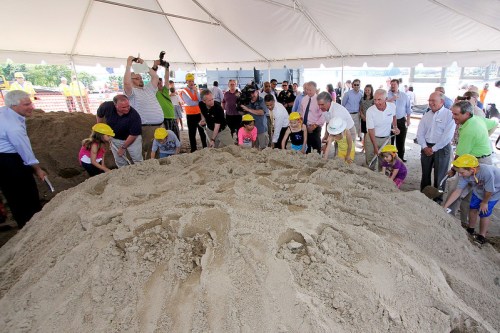 A group of people, including children, gather under a tent to dig into a large pile of sand during a ceremony.