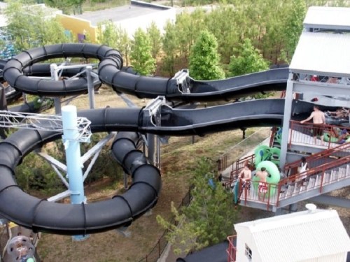 Aerial view of a water slide complex with two black slides and a loading area surrounded by greenery.