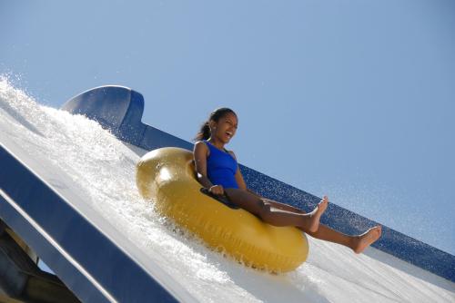 A child in a blue swimsuit joyfully slides down a water slide on a yellow inner tube, splashing water around.