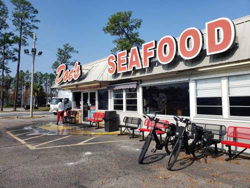 Exterior of Doc's Seafood restaurant with red signage, benches, and bicycles parked outside on a sunny day.