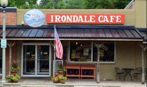 Exterior of Irondale Cafe featuring a sign, American flag, and potted plants on a sunny day.
