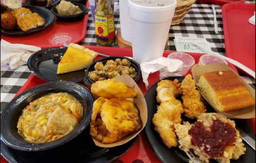 A colorful plate of Southern comfort food, including fried chicken, cornbread, greens, and a slice of cake on a red tray.