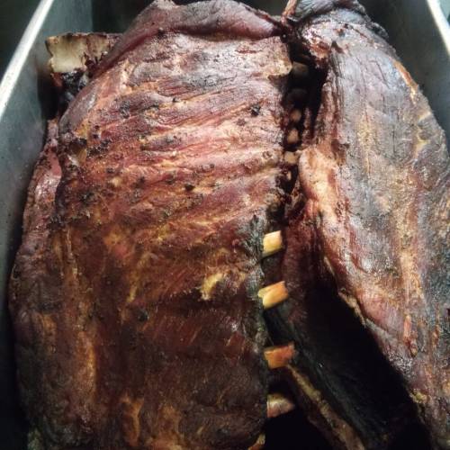 Close-up of smoked, barbecued ribs in a metal tray, showcasing a rich, dark crust and visible bones.