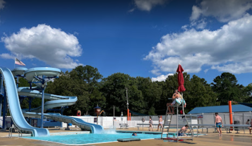 A sunny pool scene featuring water slides, a lifeguard on duty, and people enjoying the water.