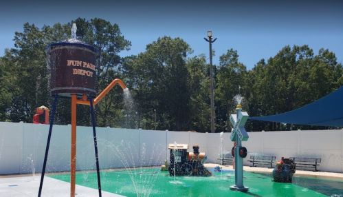 A colorful water play area featuring a large water tower, spray features, and a green splash pad under a blue sky.