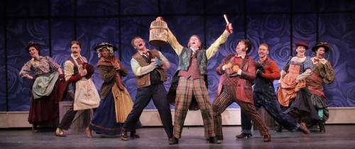 A lively musical performance with a group of actors in colorful costumes, joyfully singing and dancing on stage.