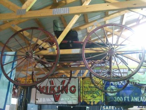 A vintage horse-drawn carriage suspended from a wooden ceiling, surrounded by colorful banners.