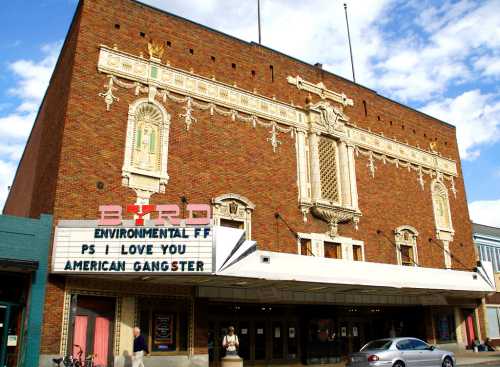 Historic theater facade with a marquee displaying "Environmental F.F., PS I Love You, American Gangster." Blue sky above.