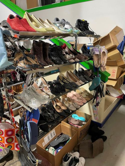A cluttered display of various shoes on shelves, with boxes and bags scattered on the floor nearby.
