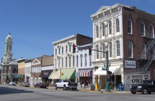 Historic downtown street with charming buildings, shops, and a clock tower under a clear blue sky.