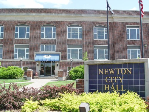 Exterior view of Newton City Hall, featuring a brick building with large windows and a sign in front.