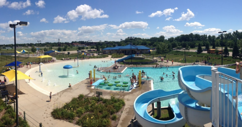 A sunny water park scene featuring slides, a pool, and people enjoying the water and surrounding areas.