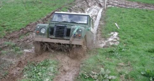 A green off-road vehicle struggles through muddy terrain in a grassy field.