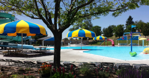 A vibrant pool area with blue and yellow umbrellas, water slides, and lounge chairs surrounded by greenery.