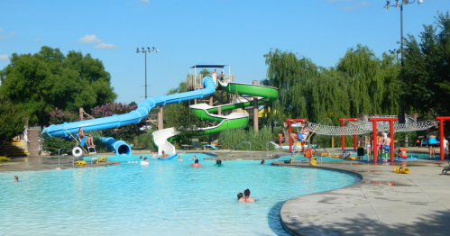 A vibrant water park scene with slides, a pool, and people enjoying the sun and water activities.