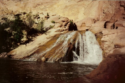A waterfall cascading over rocky terrain into a serene pool, surrounded by earthy cliffs and greenery.