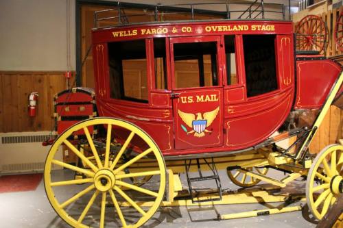A vintage Wells Fargo stagecoach in red and yellow, marked "U.S. Mail," displayed in a museum setting.