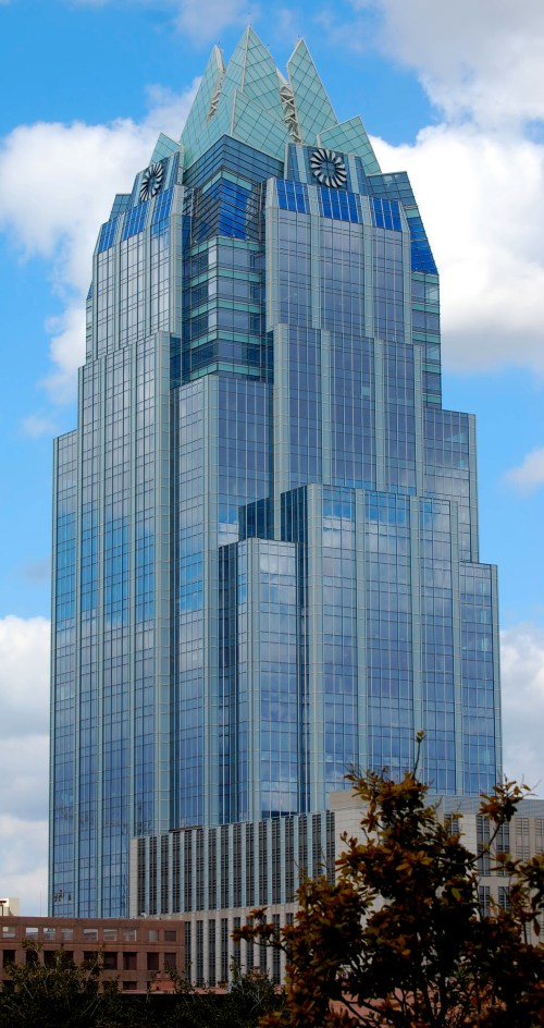 A tall, modern skyscraper with a glass facade and distinctive pointed roof against a cloudy sky.