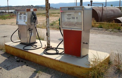 Two vintage diesel fuel pumps on a weathered concrete platform in an abandoned gas station.