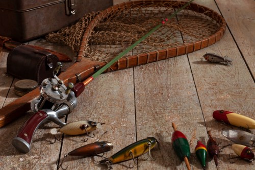 Fishing gear laid out on a wooden surface, including a rod, reel, net, and various lures.
