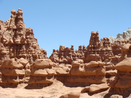 A landscape of unique red rock formations under a clear blue sky, showcasing natural sculptures and rugged terrain.