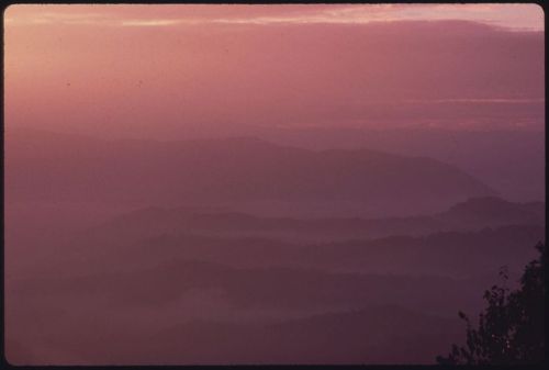 A misty mountain landscape at dawn, with soft purple and pink hues in the sky.