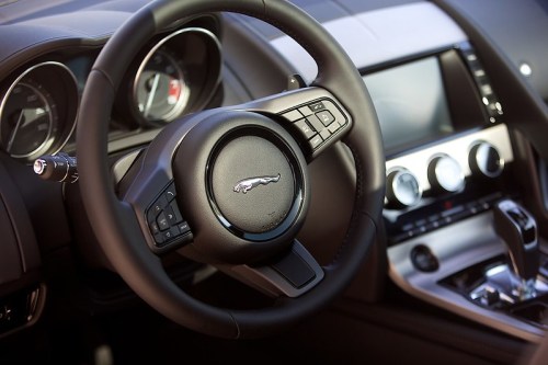 Close-up of a luxury car's steering wheel and dashboard, featuring the Jaguar logo and modern controls.