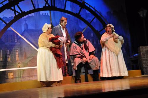 A theatrical scene with four actors in period costumes, performing on stage with a large clock backdrop.