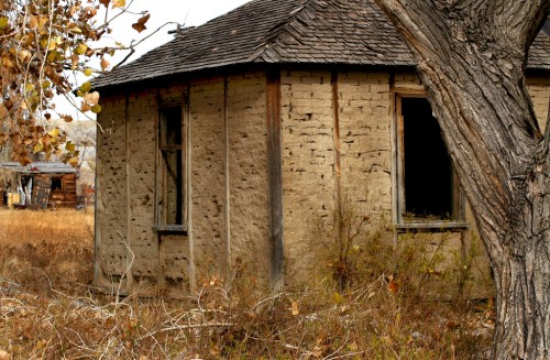 Abandoned round building with weathered walls, surrounded by overgrown grass and trees.