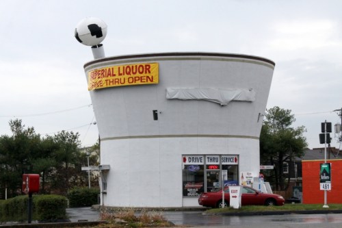 A unique liquor store shaped like a cup, featuring a drive-thru and a large soccer ball on top.