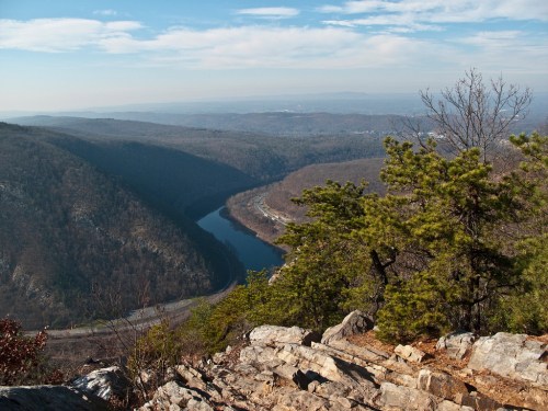 A scenic view of a winding river surrounded by mountains and trees under a clear blue sky.