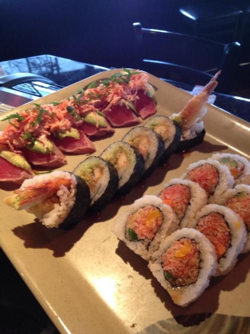 A plate of sushi featuring various rolls, including shrimp, tuna, and colorful toppings, garnished with green onions.