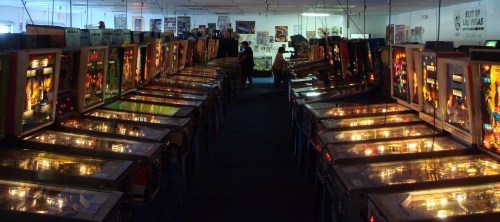 A dimly lit arcade filled with rows of vintage pinball machines, showcasing colorful lights and displays.
