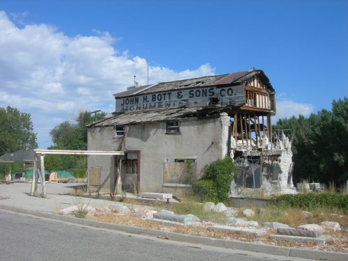 Abandoned building with a partially collapsed roof, featuring a sign for "John H. Bott & Sons Co. Monument."