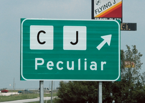 Green highway sign indicating "CJ Peculiar" with an arrow pointing right. A travel plaza sign is visible in the background.