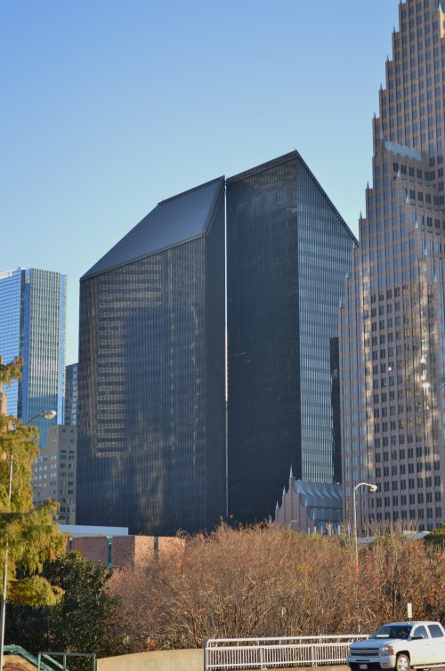 Two tall, modern skyscrapers with dark glass facades, surrounded by trees and other buildings in an urban setting.