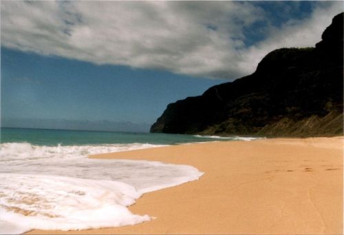 A serene beach with golden sand, gentle waves, and a backdrop of rocky cliffs under a partly cloudy sky.