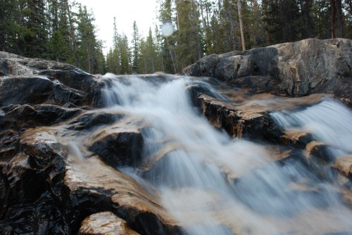 A serene waterfall cascading over rocky terrain, surrounded by lush green trees in a natural setting.