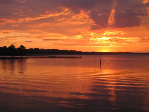 A vibrant sunset over a calm lake, with colorful clouds reflecting on the water and a pier in the foreground.