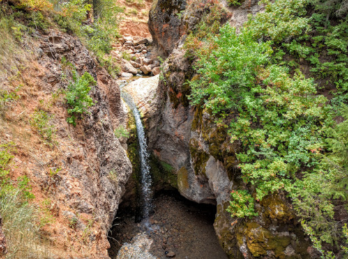 A small waterfall cascades between rocky cliffs, surrounded by lush green vegetation.