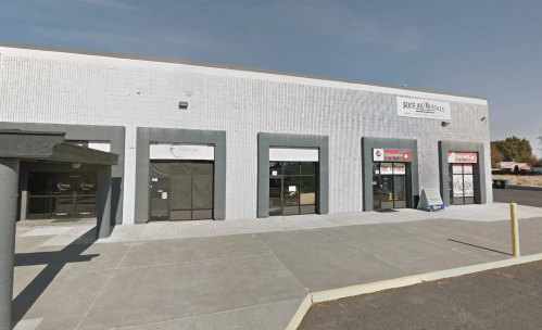 Exterior view of a commercial building with multiple storefronts, featuring large windows and a gray facade.