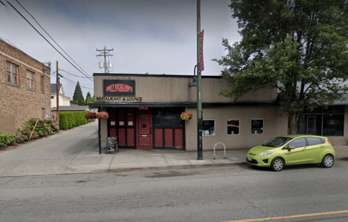 A restaurant and lounge with a red door, surrounded by greenery, and a green car parked in front.