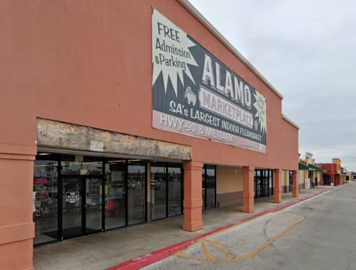 Exterior of Alamo Marketplace, featuring a large sign and storefront with open doors, under a cloudy sky.