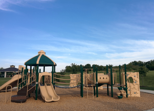 Playground with slides, climbing structures, and a grassy area under a clear blue sky.