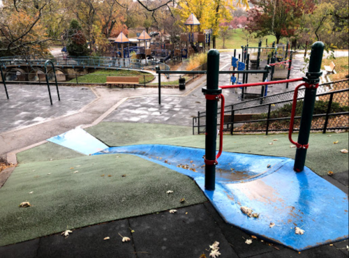 A playground slide with a blue surface, surrounded by green grass and trees, in a park setting.
