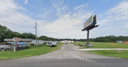A rural road intersection with a billboard, RVs, and a grassy area under a partly cloudy sky.