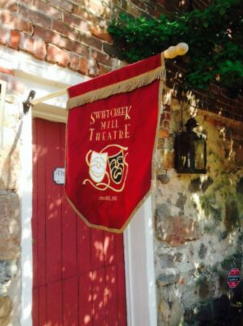 A red banner with gold trim displaying "Swift Creek Mill Theatre" and comedy-tragedy masks, hanging by a door.