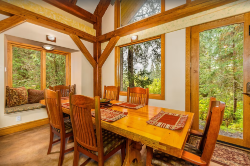 A cozy dining area with a wooden table, chairs, and large windows overlooking a forested view.