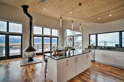 Modern kitchen with a large island, wooden floors, and panoramic windows showcasing a mountain view.