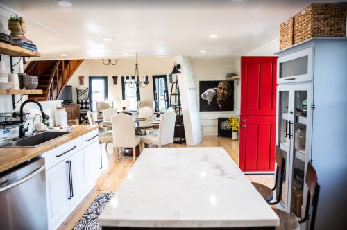 A modern kitchen and dining area with a marble countertop, white cabinets, and a striking red door.